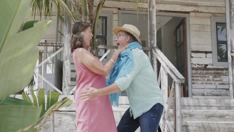 una feliz pareja caucásica se divierte bailando fuera de una casa de playa de madera, en cámara lenta