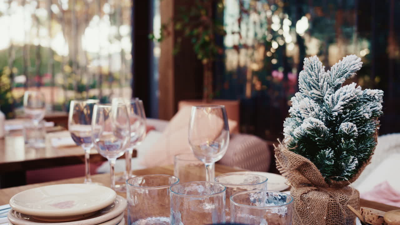 Cozy table setting with glassware and a small snow covered Christmas tree decoration at a resturant
