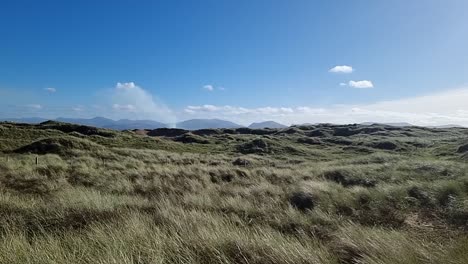 Slow-motion-panning-across-grassy-sand-dune-landscape-with-misty-Snowdonia-mountain-range-on-sunrise-horizon