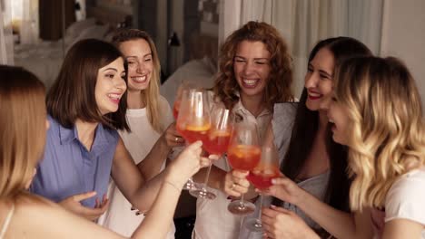 Six-girls-standing-in-a-close-circle-and-communicating.-Celebrating,-drinking-beverages-from-glasses.-Cheers.-Indoors.-Bright,-fancy-interior.-High-angle-footage