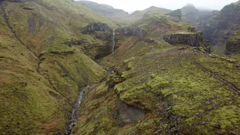 Auténtico-Paisaje-Aéreo-De-Las-Tierras-Altas-De-Islandia,-Cascada-En-El-Desierto-De-Empinadas-Colinas-Volcánicas-Y-Montañas-Con-Senderos-Para-Caminatas