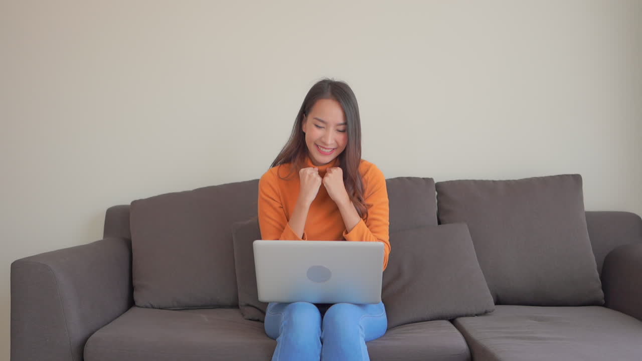 Happy woman exults while at computer on sofa. Slow motion