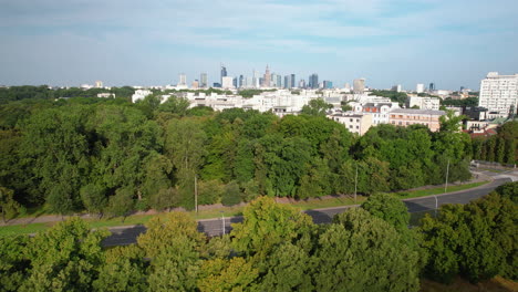 aerial backwards shot of road and forest in suburb area of warsaw city and skyline in background