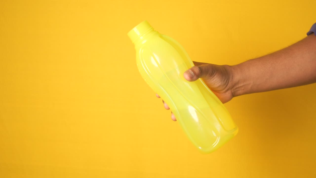 persona sosteniendo una botella de agua de plástico amarilla contra un fondo amarillo