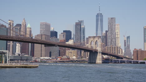 Distrito-Financiero-De-Manhattan-Con-El-One-World-Trade-Center-Y-El-Puente-De-Brooklyn-En-Un-Día-Soleado,-Toma-Estática-Desde-La-Orilla-Del-Río-Este