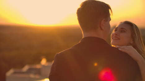 a man and a woman in love dance standing on the roof of a building at sunset looking at each other.