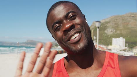 Portrait-of-smiling-african-american-man,-waving-to-camera,-taking-break-in-exercise-outdoors