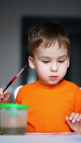 serious focused kid bit his lip during the creative process of painting. lovely child doing art at home. close up. vertical video.