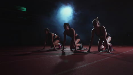 female runners at athletics track crouching at the starting blocks before a race. in slow motion.