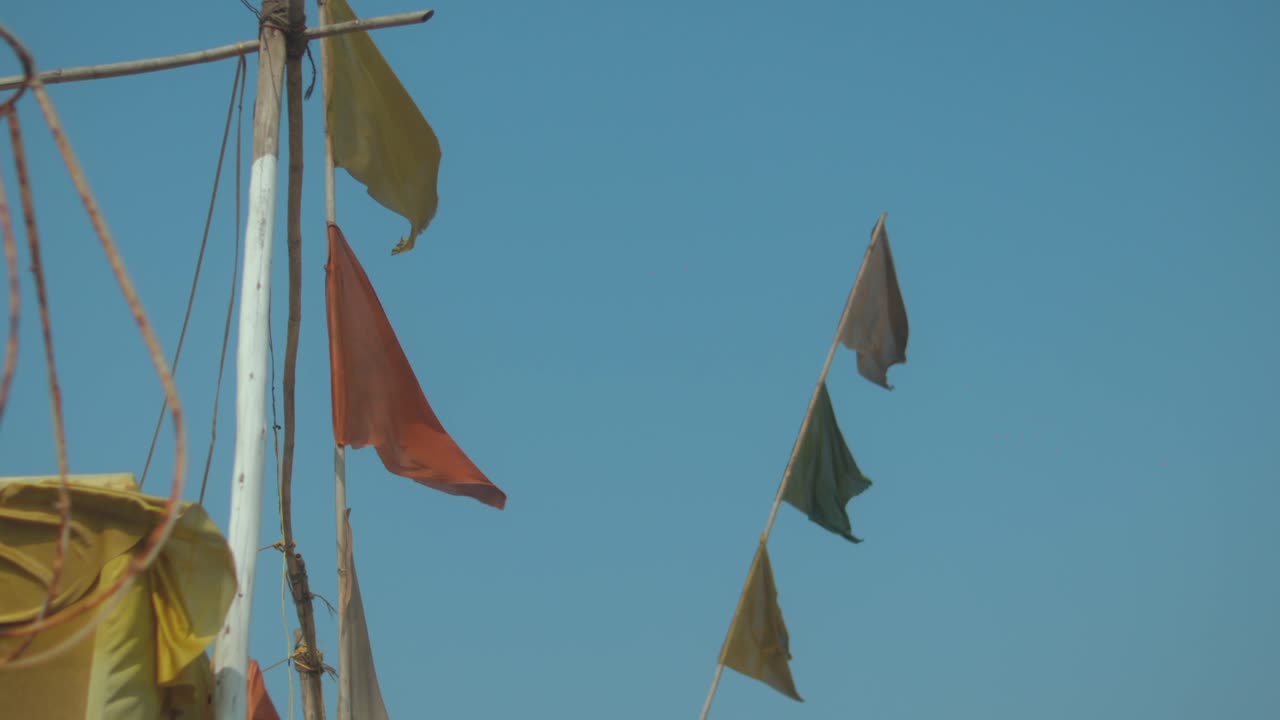 Bright fabric flags wave in steady wind on tall pole with clear blue sky background