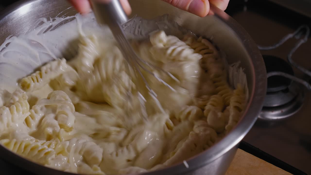 usando un batidor para mezclar la pasta fusilli y la masa de queso, haciendo pastel de queso - tiro constante
