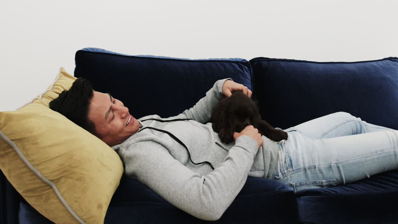Relaxing on couch, Asian man smiling while petting dog at home