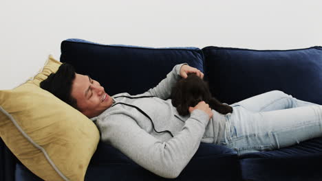 relaxing on couch, asian man smiling while petting dog at home