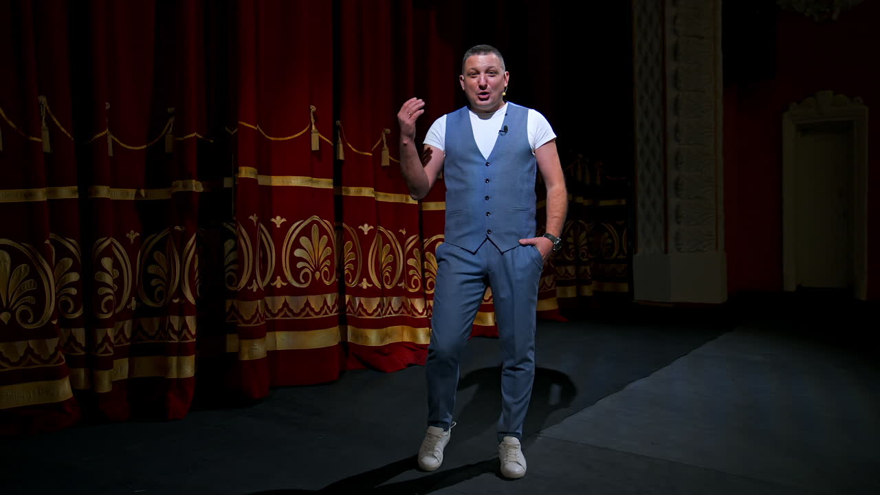 Man in suit speaking jokes in microphone standing on stage. Funny performance. Comedian in good humor speaks to the audience.