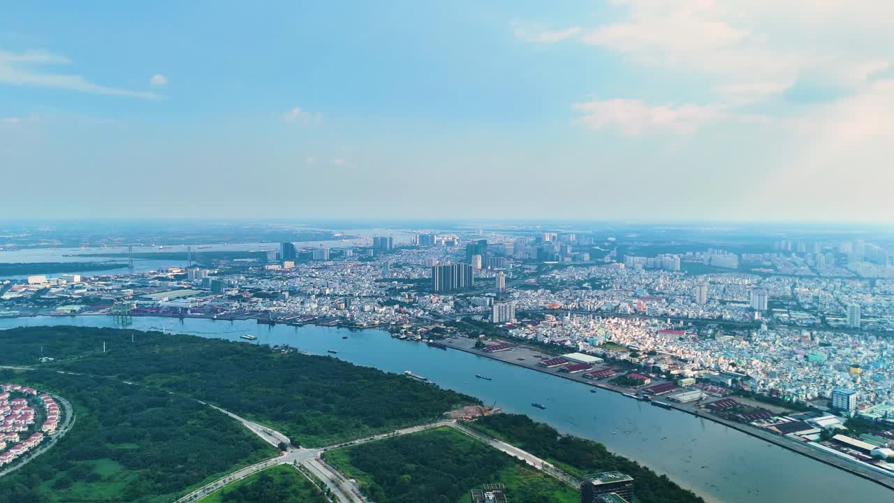 A daytime aerial view of Ho Chi Minh City with the Saigon River winding through the urban sprawl reveals a contrast between the dense cityscape and lush greenery. Vietnam, UHD.
