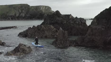 Paddleboarder-Im-Neoprenanzug-Im-Gefährlichen-Ozeanchaos-In-Der-Nähe-Von-Schroffen-Felsen