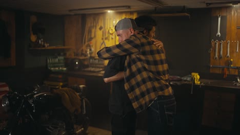 Happy-brunette-guy-and-a-mechanic-in-a-checkered-shirt-shake-hands-after-successfully-fixing-a-motorcycle-in-a-workshop