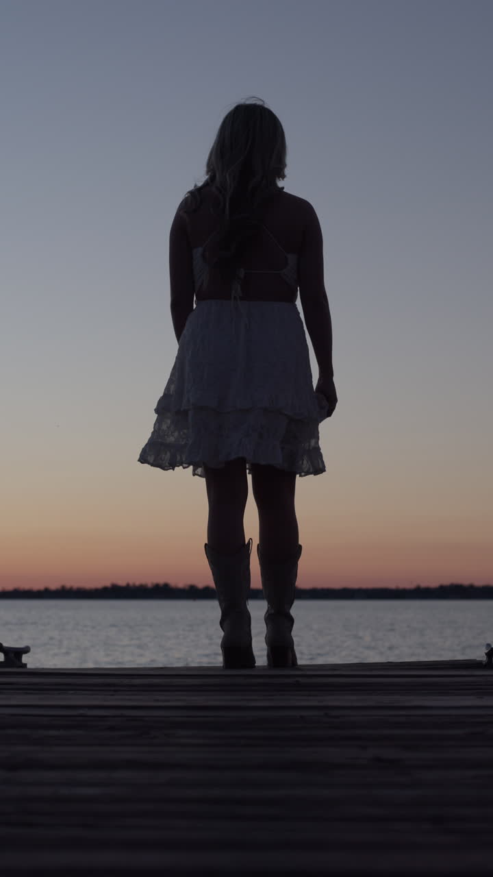 Silhouette di una bella ragazza che cammina su un molo al tramonto indossando un vestito bianco
