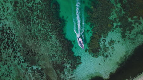 top down drone of boat navigating narrow channel between reef and lush island