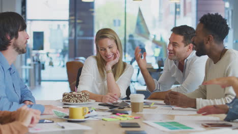 colleagues celebrating businesswoman's birthday at meeting around table in modern open plan office