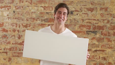 caucasian man holding a white rectangle on a brick wall