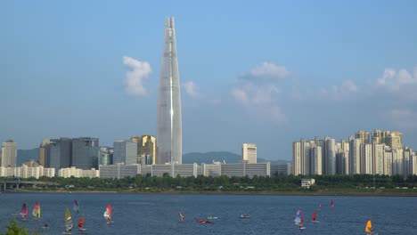 people doing water sports on han river - windsurfing, kayaking, paddleboarding, riding a canoe, water ski - lotter world tower on background on a beautiful sunny day, jamsil,seoul, south korea