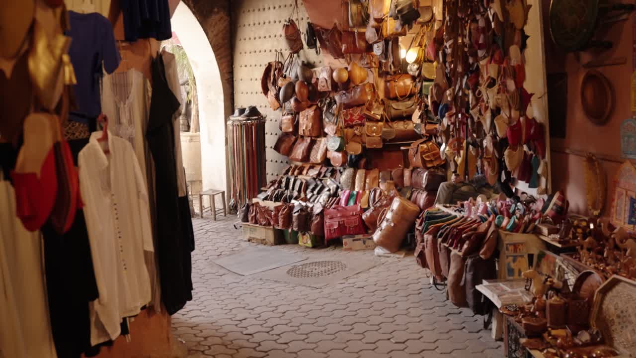 Leather bags, belts, and shoes are displayed in a traditional Moroccan souk stall under warm light