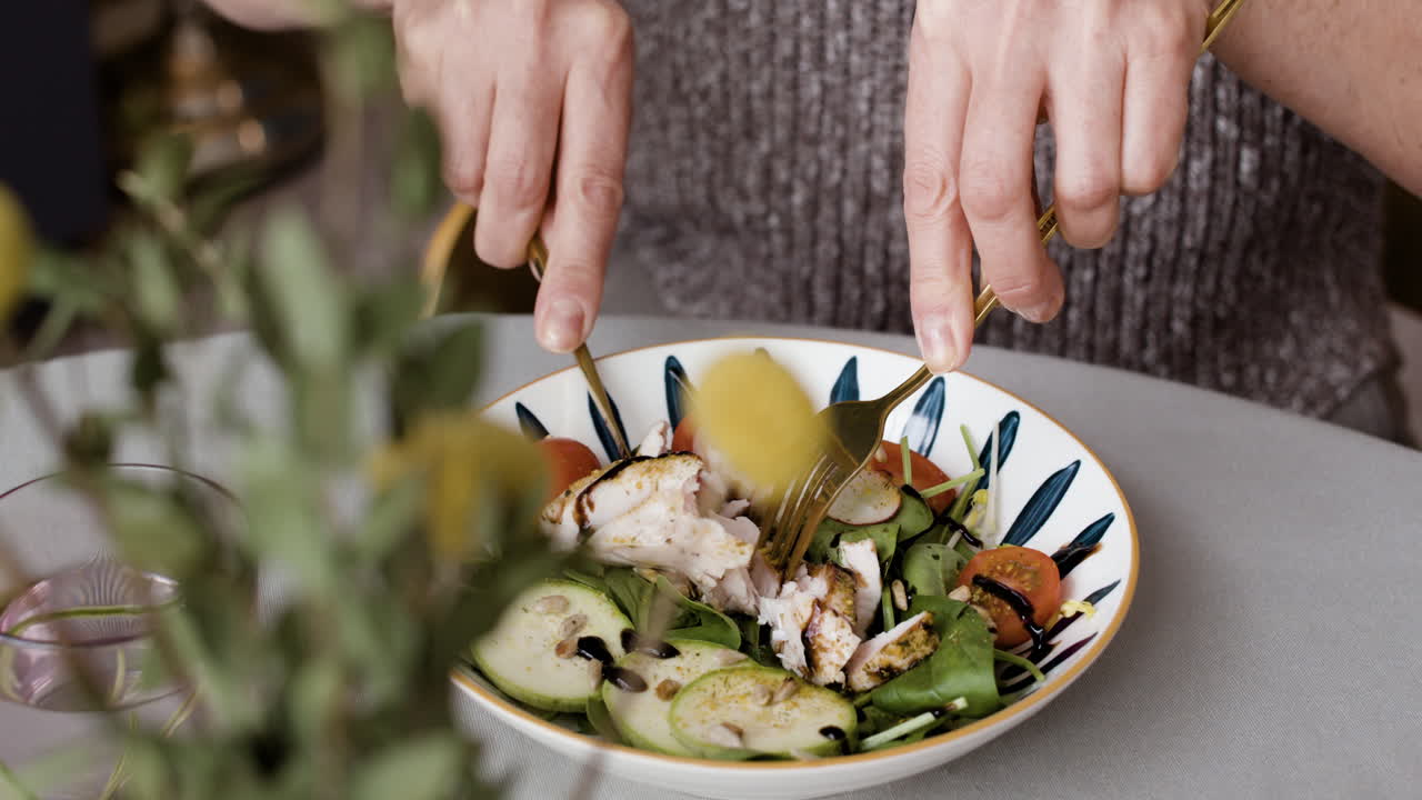 Close-up of a person eating a fresh salad with chicken and vegetables