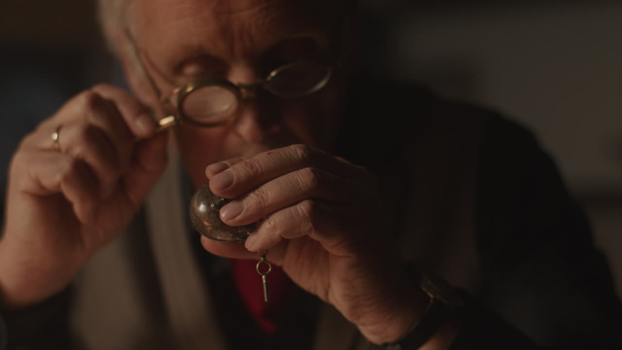 Older passionate man evaluates an old silver skull watch in his office at night