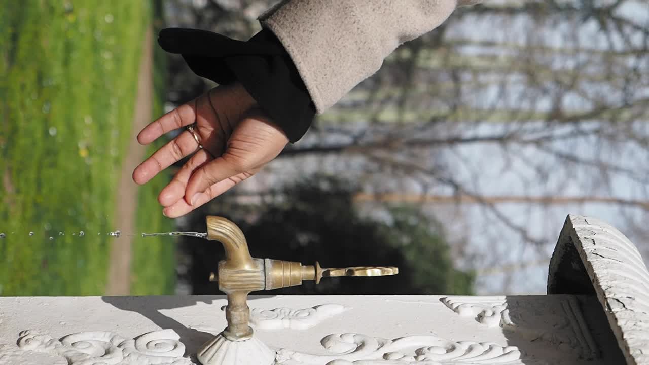 Person drinking water from a vintage outdoor fountain in a park