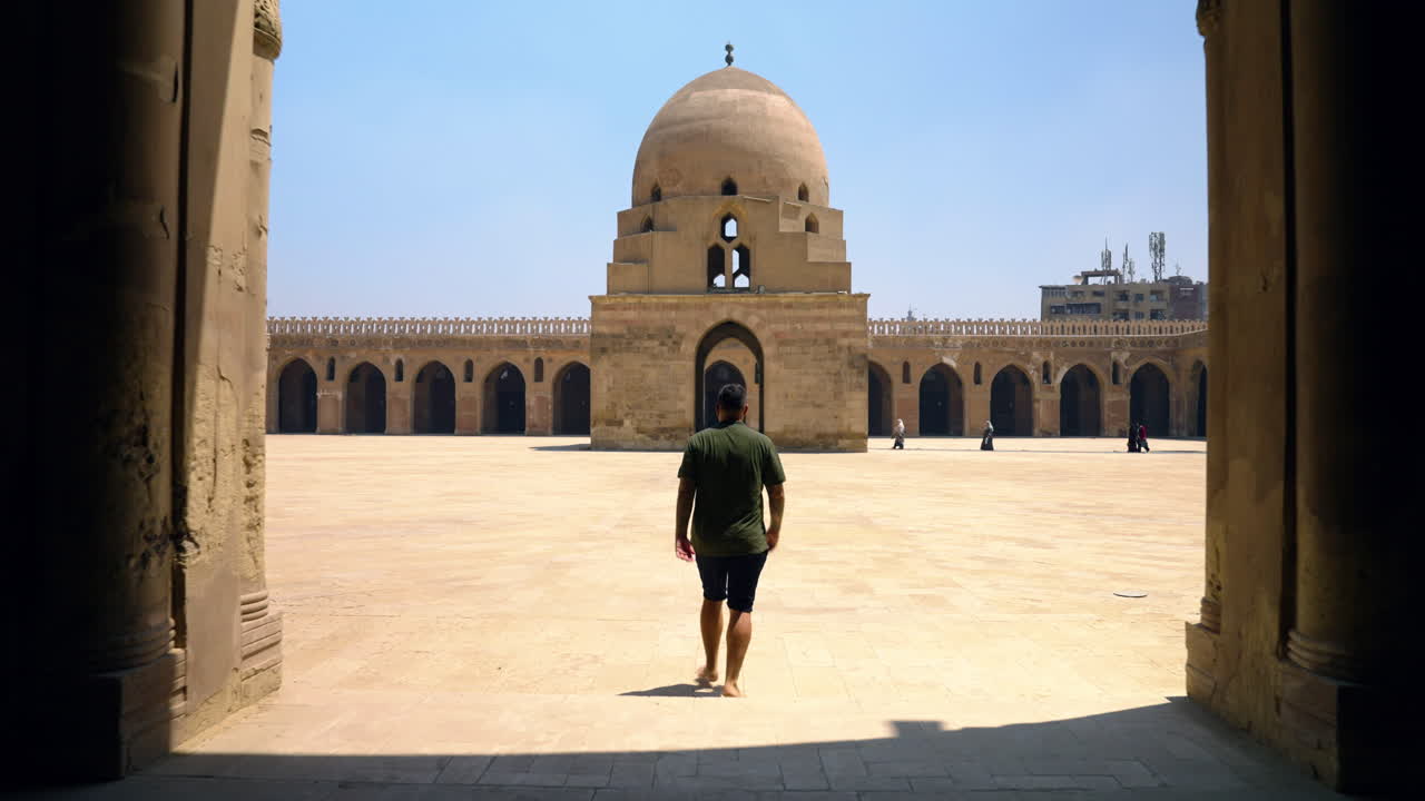 hombre entrando en el patio interior cuadrado de la mezquita ibn tulun en el cairo, egipto.