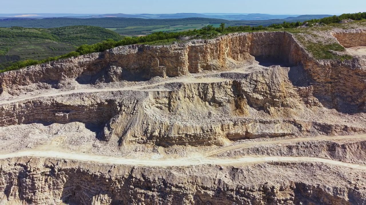 Kırsal bir alanda, gündüz vakti, arka planda açık gökyüzüyle kireçtaşı ocağı faaliyetini gösteren inşaat alanı.