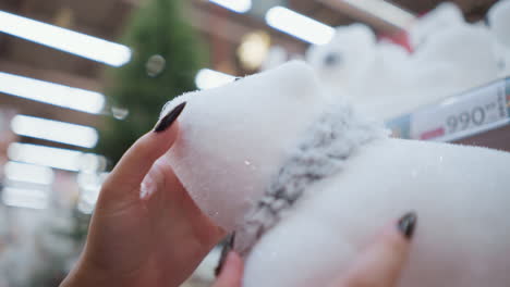 primer plano de la mano con uñas pulidas negras tocando suavemente el oso polar de peluche con textura suave, fondo borroso con luces bokeh y productos de la tienda que crean una atmósfera festiva