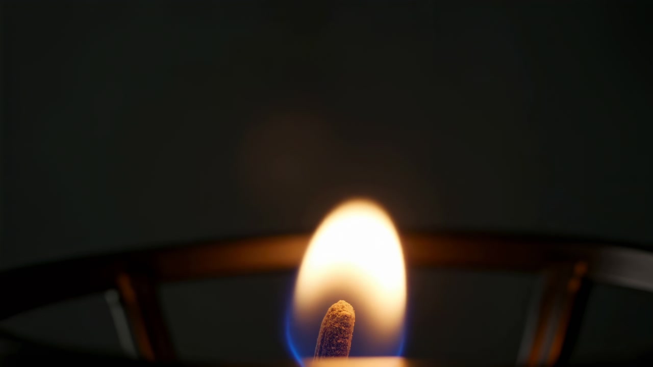 Fiamma costante, su sfondo scuro, con candela, con texture di cera, da una prospettiva ravvicinata, con accenti arancioni e blu, e un'atmosfera calda e serena, con luce chiara e composizione equilibrata.