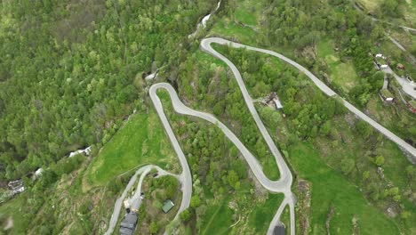 winding geiranger road coming down from the mountains and to the village of geiranger - aerial looking down at winding road while rotating and tilting up in the end