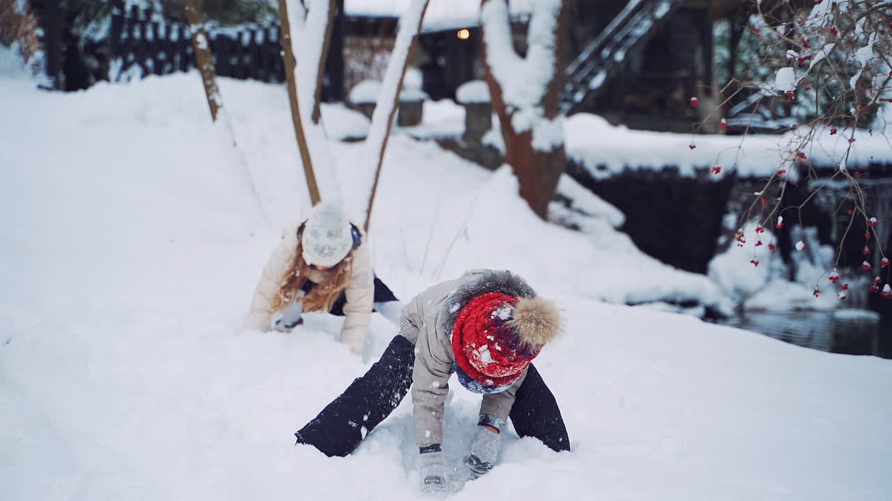 Cheerful children are throwing soft snow on the background of winter river. Little kids are playing happily with white snow in winter in the forest. Slow motion.