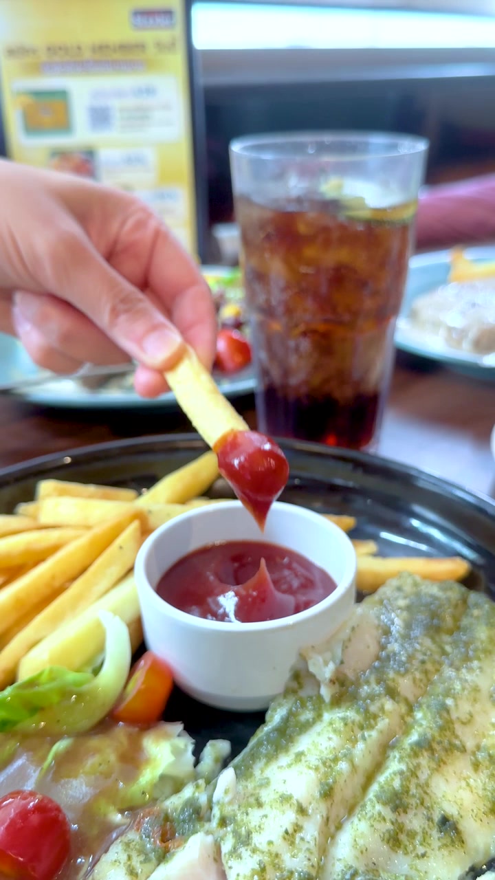 Primo piano di una mano che intinge una patatina fritta nella salsa rossa durante la cena.