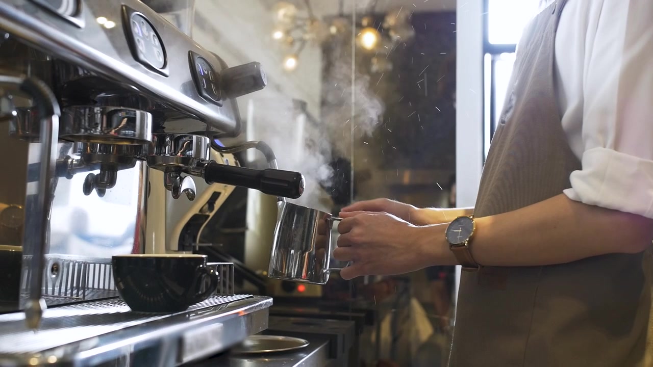 Un barista con grembiule marrone in una caffetteria alla moda gira la manopola della macchina per espresso per erogare il caffè per una bevanda calda. Movimento lento, carrellata a sinistra.