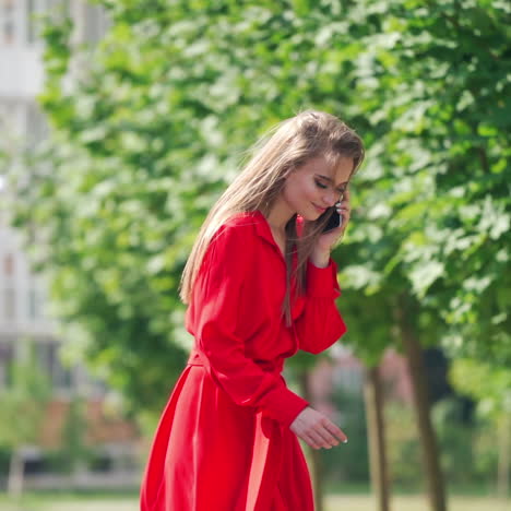 gorgeous long-haired woman in red dress. attractive lady talking the mobile phone on the city background in a bright summer day. slow motion.