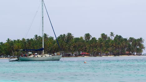 a sailboat calmly drifts in front of a san blas island, with overcast skies and serene caribbean waters