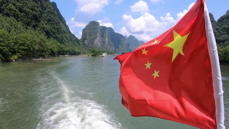red chinese national flag fluttering on a mast on the deck of sightseeing boatt full of tourists departing on a trip on the magnificent li river from guilin to yangshuo, china