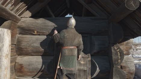 medieval knight in armor outside a wooden hut