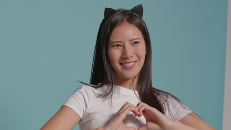푸른 스튜디오 배경 앞에 있는 젊은 여성이 옷을 입고 사진 부스 스타일의 초상화를 위해 포즈를 취하고 있습니다.