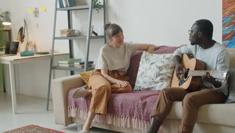 happy multiethnic couple singing to guitar at home