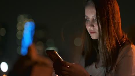 una joven turista viaja por la megalópolis nocturna y escribe mensajes de texto en las redes sociales sobre el viaje sostiene el teléfono en sus manos y mira la pantalla del gadget