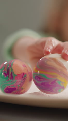 child puts easter egg with vibrant ebru design patterns onto plate at home closeup slow motion. symbol of spring christian holiday celebration