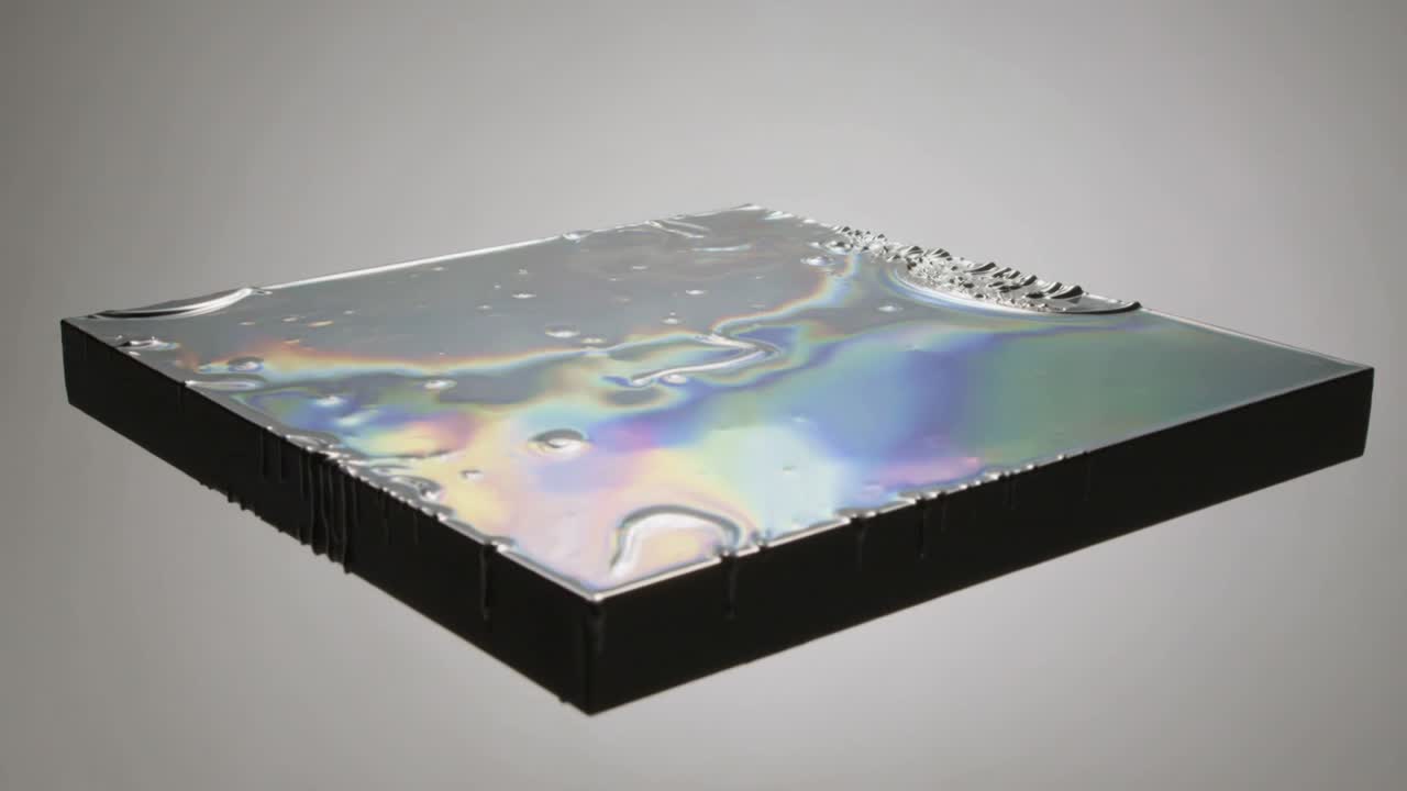 Developing disturbance on iridescent film covering black platform, forming ridge and edge drips