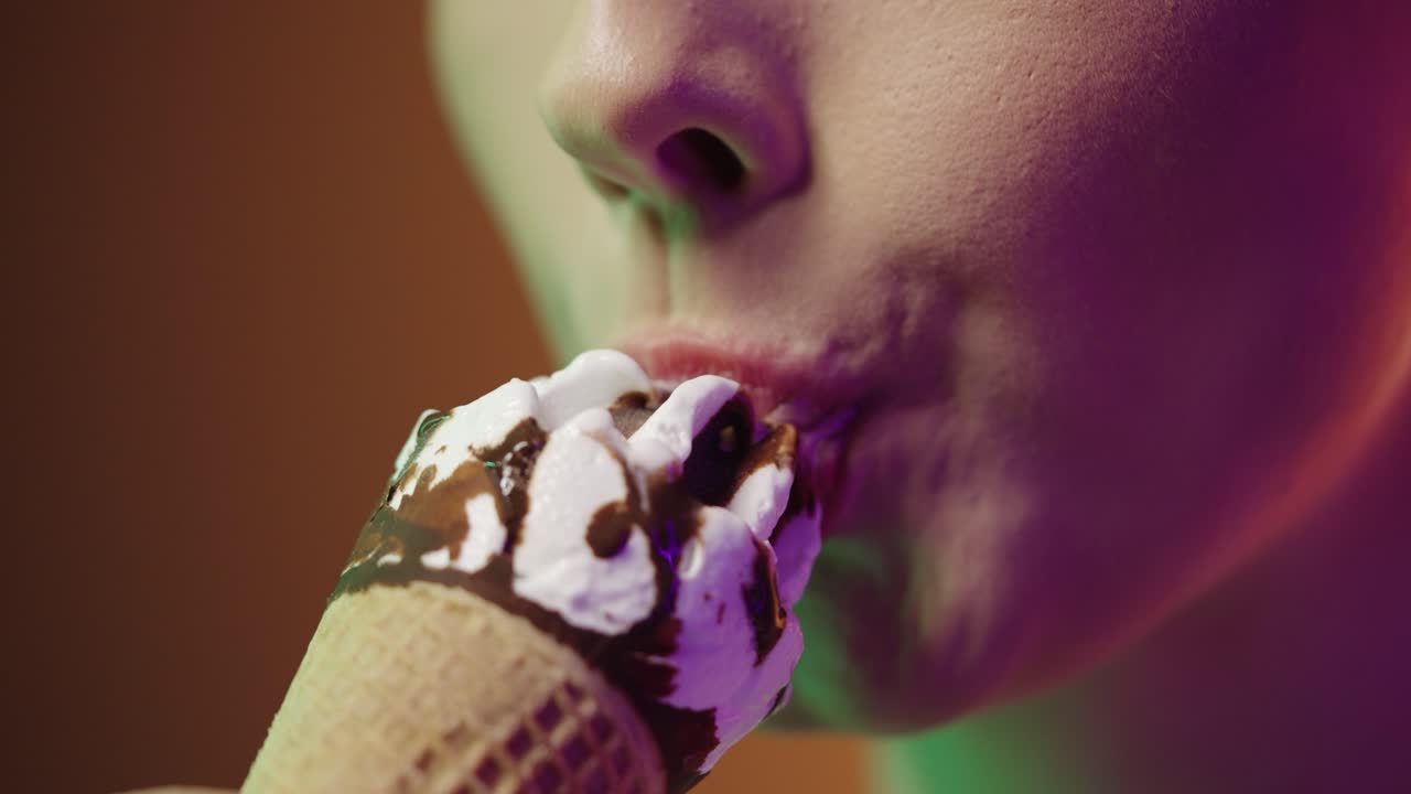 Close up of a young woman eating a vegan cream ice cream with vegan chocolate and enjoying the delicious taste in front of black and yellow background in slow motion