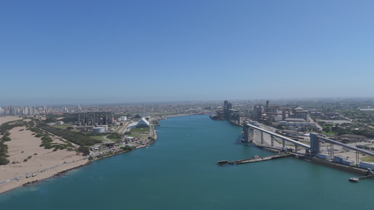 Expansive aerial footage rising above the Port of Necochea, Argentina. Highlights its bustling maritime activity, industrial infrastructure, and stunning views of the surrounding coastline.