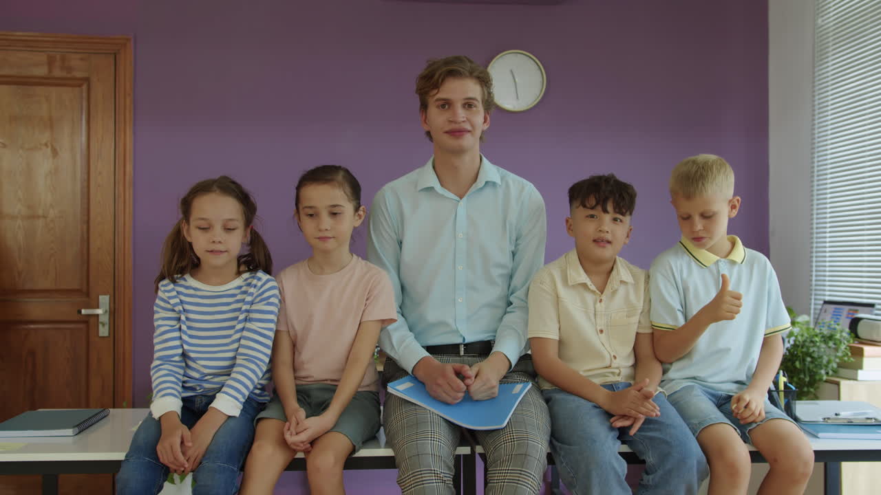Portrait of Diverse Schoolkids and Young Teacher Sitting on Desk in Classroom